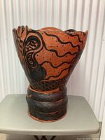 Front view of the large vintage clay pot with snake design painted in black on reddish-brown clay. Shows scalloped pot edge and some surface wear.