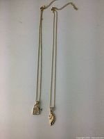 Two gold-tone vintage costume jewelry necklaces, one with a padlock and key pendant, the other with a wing pendant.