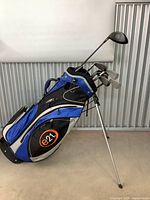 Photo showing full golf club set in e21 blue, black and white golf bag with clubs inside and metal legs extended.