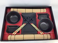 Top-down view of all sushi set items arranged in their box including bowls, plates, chopsticks, and bamboo mats.