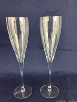 Pair of clear crystal champagne flutes standing upright against a dark blue background, showing overall shape and proportion.
