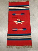 Full view of red Chimayo tapestry runner with arrow and thunderbird designs, showing fringe and color patterns.