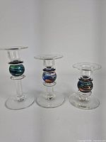 Front view of the set of three hand blown glass candle holders showing fiery colored orbs in the middle with clear glass stems and bases.