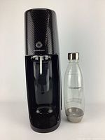Full frontal view of black SodaStream carbonated drink maker with clear bottle placed beside it, showing general condition and size.