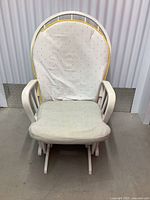 Front angled view of the white wooden gliding rocking chair with cream and polka dot cushions, showing wear and stains.