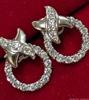 Front view of pair of 10KT gold earrings with CZ circular hoops and abstract CZ-embellished tops on red background.