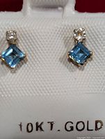 Front view of earrings showing blue square-cut stones with small round diamonds on top, mounted in 10KT gold on white backing with '10KT GOLD' marking