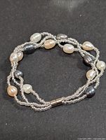 Photo showing multi-strand bracelet with fresh water pearls of varied colors and silver magnetic clasp on black background.