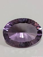 Oval shaped light to medium purple faceted amethyst gemstone on white background showing pavilion facets and polished surface.