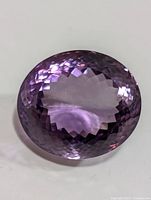 Close-up image showing the multi-faceted checkerboard cut on the top surface of the oval amethyst gemstone, highlighting color and clarity.