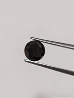 Close-up image of the loose black diamond gemstone held in tweezers showing its round cut and faceted surface.