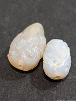 Two carved genuine opal stones showing detailed carvings and drilled holes on black background