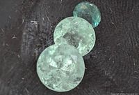 Close-up photo of the three Columbian emerald gemstones showing natural blue-green color and inclusions.