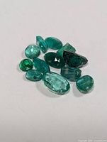 Loose genuine emerald gemstones of various shapes and shades on a white background.
