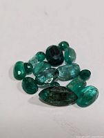 Close-up photo showing loose green emerald gemstones of various shapes and sizes on a white background.