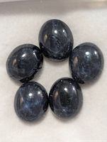 Photo showing five oval polished dark blue enhanced star sapphire gemstones arranged in a circular pattern to display their asterism features.