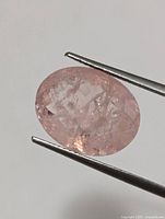 Oval cut genuine morganite gemstone held with tweezers, showing slight internal inclusions and pink coloration.