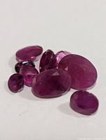 Photo showing several genuine ruby and sapphire apx 5.5ct gemstones laid on white background, various shapes and cuts.