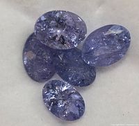 Close-up view of five loose oval tanzanite gemstones on white fabric showing color and inclusions.