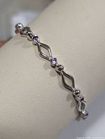 Close-up view of the silver bracelet showing amethyst stones and wave link design on cream background.