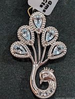Front view photo of silver peacock-shaped pendant with five pear-shaped faceted blue topaz stones and detailed silver bead outline