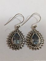 Pair of silver earrings with pear-shaped blue topaz gems, displayed flat on white background.