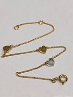Close-up view of the bracelet chain with gold tone hearts and one silver heart charm, showing clasp and charm detail.