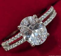 Close-up photo of silver ring with oval CZ center stone on a red background