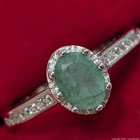 Close-up of the ring face showing oval emerald surrounded by cubic zirconia accents and band detail.