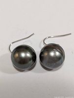 Front view of two silver hook earrings with large dark round freshwater pearls attached, showing natural pearl luster and slight surface texture.