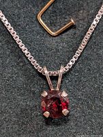 Close-up top view of silver necklace chain and garnet pendant showing the faceted gemstone and silver prong setting.
