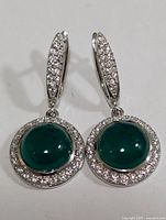 Front view of the pair of silver earrings with green onyx and clear cubic zirconia stones in round drop design.