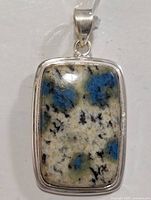 Front view of rectangular silver pendant featuring a polished K2 Jasper stone with blue, white, and black patterns.