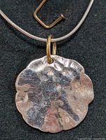 Close-up of front side of silver round hammered pendant on thin silver chain with gold-tone bail