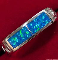 Close-up of silver ring with bright blue and green opalite inlay showing detail and color variations, highlighting rectangular double-stone design and silver band sides.