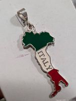 Front view of silver pendant shaped like the map of Italy, decorated with green, white, and red enamel colors representing the Italian flag, with the word 'ITALY' on the white section.