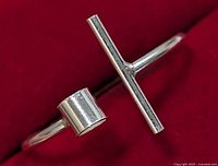 Silver open-ended ring with horizontal bar and cylindrical end viewed from side on a red background.