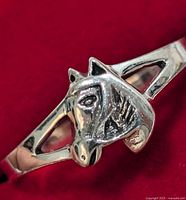 Close-up image showing the front of the silver ring with horse head detail on a red background.