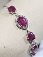 Close-up of silver bracelet showing deep red oval rubies and clear cubic zirconia stones in teardrop surrounds on silver chain.