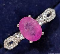 Close up photo of the silver ring with oval ruby and cubic zirconia stones on a dark blue background