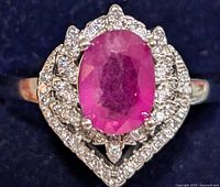 Front close-up of silver ring with oval ruby and surrounding cubic zirconia stones.