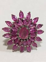 Front view of silver ring showing concentric arrangement of marquise-shaped pink/red rubies with an oval ruby center, flower motif