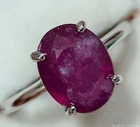 Close-up of the silver ring with an oval-shaped ruby gemstone from one angle showing prong setting and stone surface details.