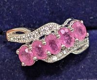 Close-up front side view of silver ring displaying five oval pink rubies aligned horizontally with clear accent stones on band.