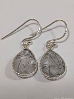 Front-facing view of silver earrings with rutilated quartz teardrop stones showing needle inclusions and textured silver bezels.