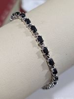 Close-up photo showing dark blue oval sapphires set in polished silver linked bracelet worn on display full circumference visible