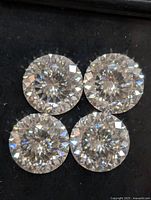 Close-up of four round-cut moissanite stones showing brilliance and cut facets on black background