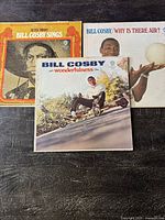 Three Bill Cosby album vinyl covers: Silver Throat, Why Is There Air?, and Wonderfulness laid out on dark surface.