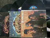 Three vinyl records and their album covers laid out on a dark surface: two The Commodores albums and one The Ventures album.