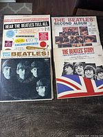 Four Beatles vinyl albums arranged flat showing covers: Meet The Beatles!, The Beatles' Second Album, The Beatles' Story, Hear The Beatles Tell All, with visible wear and aging on covers.